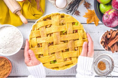 Sonbahar elmalı turta pişirme geçmişi. Çiğ geleneksel elmalı turta, fırın malzemeleri ve çatal bıçaklar, beyaz arka plan fotokopi alanı, kız eli pastayı tutuyor. 