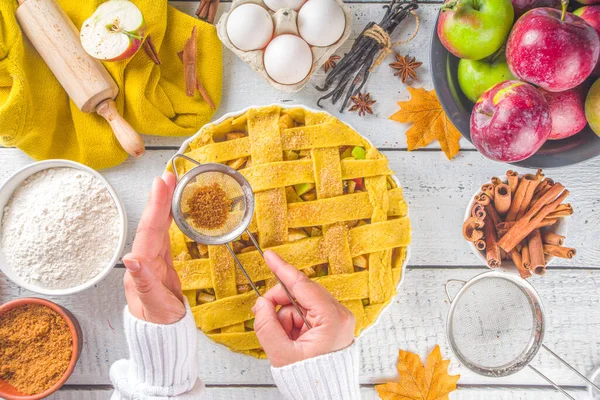Sonbahar elmalı turta pişirme geçmişi. Çiğ geleneksel elmalı turta, pişirme malzemeleri ve çatal bıçak, beyaz ahşap arka plan fotokopi alanı, kız elleri pasta baharatları serpiyor.