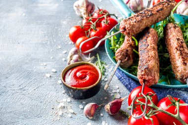 Şişe şiş kebap, kıyma etinden. Lula kebap, geleneksel Kafkas tarifi. Mavi beton arka planda, soslar, domatesler ve sebze salatası üst görünüm fotokopi alanı