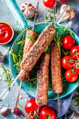 Şişe şiş kebap, kıyma etinden. Lula kebap, geleneksel Kafkas tarifi. Mavi beton arka planda, soslar, domatesler ve sebze salatası üst görünüm fotokopi alanı