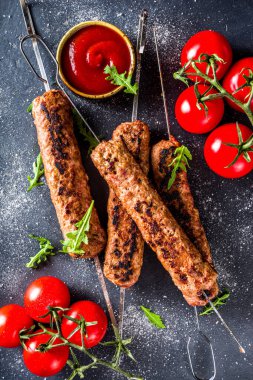 Şişe şiş kebap, kıyma etinden. Lula kebap, geleneksel Kafkas tarifi. Siyah beton arka planda, soslar, domatesler ve sebze salatası üst görünüm fotokopi alanı.