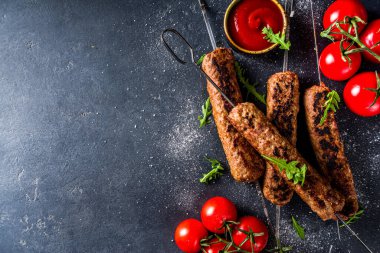 Şişe şiş kebap, kıyma etinden. Lula kebap, geleneksel Kafkas tarifi. Siyah beton arka planda, soslar, domatesler ve sebze salatası üst görünüm fotokopi alanı.