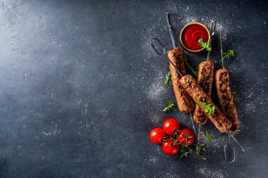 Şişe şiş kebap, kıyma etinden. Lula kebap, geleneksel Kafkas tarifi. Siyah beton arka planda, soslar, domatesler ve sebze salatası üst görünüm fotokopi alanı.