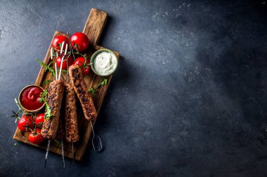 Şişe şiş kebap, kıyma etinden. Lula kebap, geleneksel Kafkas tarifi. Siyah beton arka planda, soslar, domatesler ve sebze salatası üst görünüm fotokopi alanı.
