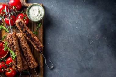 Şişe şiş kebap, kıyma etinden. Lula kebap, geleneksel Kafkas tarifi. Siyah beton arka planda, soslar, domatesler ve sebze salatası üst görünüm fotokopi alanı.