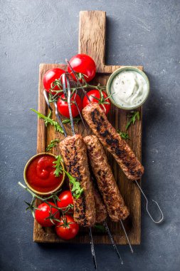Şişe şiş kebap, kıyma etinden. Lula kebap, geleneksel Kafkas tarifi. Siyah beton arka planda, soslar, domatesler ve sebze salatası üst görünüm fotokopi alanı.