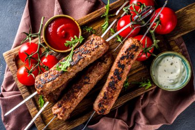 Şişe şiş kebap, kıyma etinden. Lula kebap, geleneksel Kafkas tarifi. Siyah beton arka planda, soslar, domatesler ve sebze salatası üst görünüm fotokopi alanı.