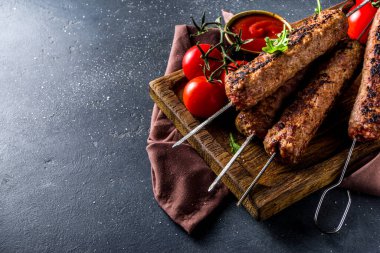 Şişe şiş kebap, kıyma etinden. Lula kebap, geleneksel Kafkas tarifi. Siyah beton arka planda, soslar, domatesler ve sebze salatası üst görünüm fotokopi alanı.