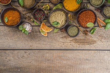 Pişirmek için baharat ve ot seti. Renkli baharatlı küçük kaseler fesleğen, biber, safran, tuz, paprika, zerdeçal. Kırsal ahşap masa arka planında, üst görünüm kopyalama alanı