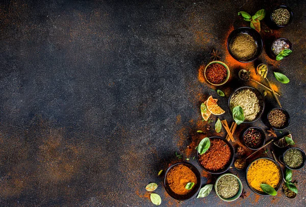 Set of Spices and herbs for cooking. Small bowls with colorful  seasonings and spices - basil, pepper, saffron, salt, paprika, turmeric. On black stone table top view copy space