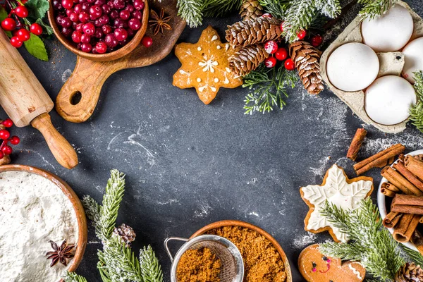 Ingredients for Christmas cooking, winter baking cookies, gingerbread, fruitcake, seasonal drinks. Cranberries, dried oranges, cinnamon, spices, flour on dark stone table, copy space top view