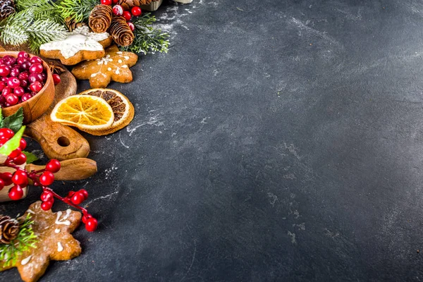 Ingredients for Christmas cooking, winter baking cookies, gingerbread, fruitcake, seasonal drinks. Cranberries, dried oranges, cinnamon, spices, flour on dark stone table, copy space top view