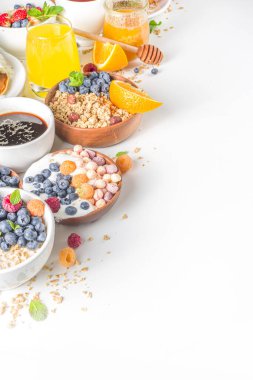 Çeşitli kahvaltı yemekleri konsepti. Geleneksel sağlıklı kahvaltı yemekleri ve içecekler - yulaf, granola, yoğurt, smoothie bowl, tost, mısır gevreği, kruvasan, kahve ve çay fincanı, portakal suyu, meyve, böğürtlen