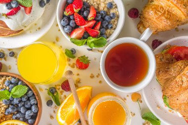 Çeşitli kahvaltı yemekleri konsepti. Geleneksel sağlıklı kahvaltı yemekleri ve içecekler - yulaf, granola, yoğurt, smoothie bowl, tost, mısır gevreği, kruvasan, kahve ve çay fincanı, portakal suyu, meyve, böğürtlen