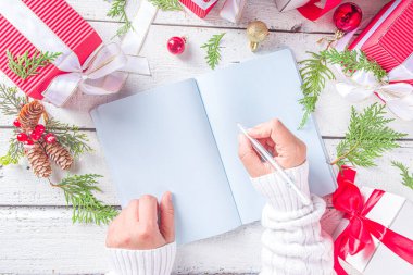 Not defterine noel süsü ve beyaz ahşap masada hediye kutuları olan bir kadın el yazısı. Noel dilek listesi, Noel Baba mektubu, liste konsepti, düz kopya alanı