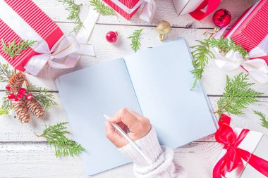 Not defterine noel süsü ve beyaz ahşap masada hediye kutuları olan bir kadın el yazısı. Noel dilek listesi, Noel Baba mektubu, liste konsepti, düz kopya alanı