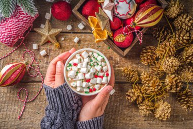 Marşmelovlu sıcak çikolata, Noel kahvaltısı için sıcak çikolata, ahşap arka planda Noel süslemeleri, samimi kış fotoğrafı. Sıcak çikolata bardağı kızların elinde. 