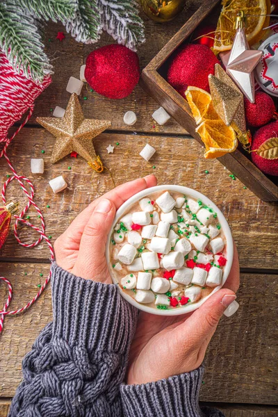 Marşmelovlu sıcak çikolata, Noel kahvaltısı için sıcak çikolata, ahşap arka planda Noel süslemeleri, samimi kış fotoğrafı. Sıcak çikolata bardağı kızların elinde. 