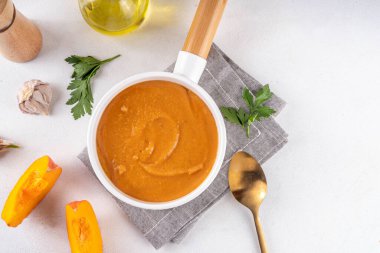 Beyaz kasede servis edilen balkabağı kremalı çorba. Geleneksel sonbahar ve kış yemekleri, sıcak ve baharatlı balkabağı çorbası, kremalı ve lezzetli, balkabağı dilimleri ve beyaz masa üzerinde bitkiler