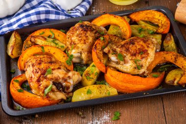 Kavrulmuş fırında tavuk budu, balkabağı ve patates dilimleri, sarımsak ve aromalı bitkiler. Lezzetli sonbahar konforlu yemekleri, Şükran Günü aile yemeği fikirleri.