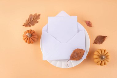 Sonbahar sofrası kurma, küçük balkabaklarıyla parti davetiyesi, güz yaprakları, tabak, çatal bıçak takımı ve bir davetiye veya selamlama ile birlikte zarf. Şükran Günü partisinin rahat arka plan fotokopi alanı