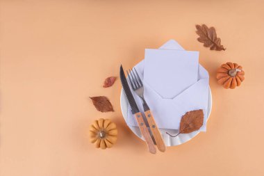 Sonbahar sofrası kurma, küçük balkabaklarıyla parti davetiyesi, güz yaprakları, tabak, çatal bıçak takımı ve bir davetiye veya selamlama ile birlikte zarf. Şükran Günü partisinin rahat arka plan fotokopi alanı