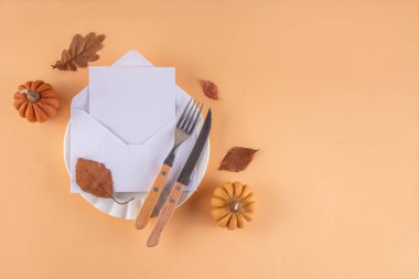 Sonbahar sofrası kurma, küçük balkabaklarıyla parti davetiyesi, güz yaprakları, tabak, çatal bıçak takımı ve bir davetiye veya selamlama ile birlikte zarf. Şükran Günü partisinin rahat arka plan fotokopi alanı