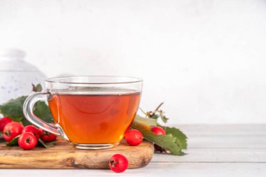 Güzel kokulu sonbahar dikenli çilek çayı. Beyaz ahşap arka planda yabani orman dikenli meyvelerden yapılan bitkisel organik sıcak içecek.