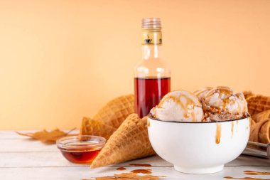 Lezzetli sonbahar akçaağaç şurubu dondurması. Akçaağaç şurubu tadında bir kase, üzerinde pekmezli çiseleme, akçaağaç yaprağı ve dondurma konileri olan dondurma, uzayı kopyala.