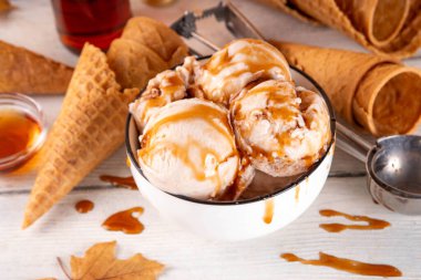 Lezzetli sonbahar akçaağaç şurubu dondurması. Akçaağaç şurubu tadında bir kase, üzerinde pekmezli çiseleme, akçaağaç yaprağı ve dondurma konileri olan dondurma, uzayı kopyala.