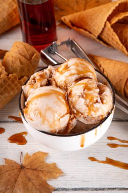 Lezzetli sonbahar akçaağaç şurubu dondurması. Akçaağaç şurubu tadında bir kase, üzerinde pekmezli çiseleme, akçaağaç yaprağı ve dondurma konileri olan dondurma, uzayı kopyala.