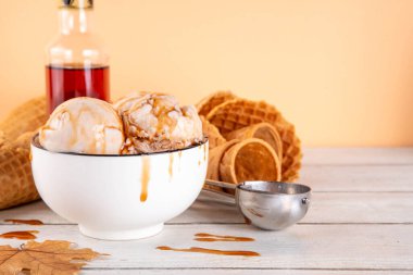 Lezzetli sonbahar akçaağaç şurubu dondurması. Akçaağaç şurubu tadında bir kase, üzerinde pekmezli çiseleme, akçaağaç yaprağı ve dondurma konileri olan dondurma, uzayı kopyala.