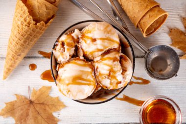 Lezzetli sonbahar akçaağaç şurubu dondurması. Akçaağaç şurubu tadında bir kase, üzerinde pekmezli çiseleme, akçaağaç yaprağı ve dondurma konileri olan dondurma, uzayı kopyala.