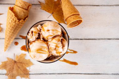 Lezzetli sonbahar akçaağaç şurubu dondurması. Akçaağaç şurubu tadında bir kase, üzerinde pekmezli çiseleme, akçaağaç yaprağı ve dondurma konileri olan dondurma, uzayı kopyala.