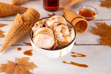 Lezzetli sonbahar akçaağaç şurubu dondurması. Akçaağaç şurubu tadında bir kase, üzerinde pekmezli çiseleme, akçaağaç yaprağı ve dondurma konileri olan dondurma, uzayı kopyala.