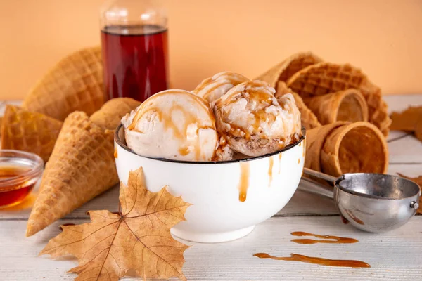 Lezzetli sonbahar akçaağaç şurubu dondurması. Akçaağaç şurubu tadında bir kase, üzerinde pekmezli çiseleme, akçaağaç yaprağı ve dondurma konileri olan dondurma, uzayı kopyala.
