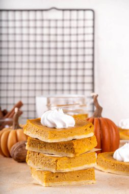 Homemade autumn taste pumpkin pie bars. Freshly baked pumpkin bars with whipped cream on it, with autumn decor and spices on beige table background, copy space 