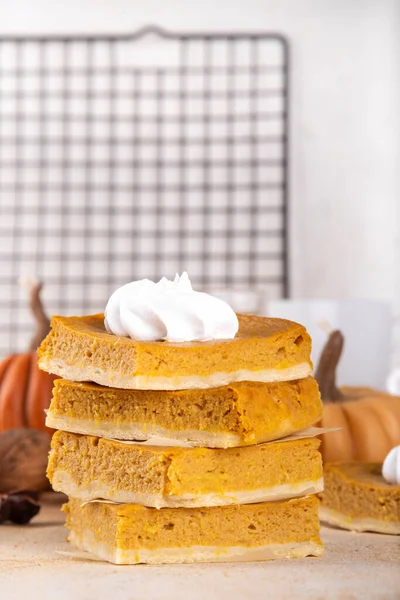 Homemade autumn taste pumpkin pie bars. Freshly baked pumpkin bars with whipped cream on it, with autumn decor and spices on beige table background, copy space 