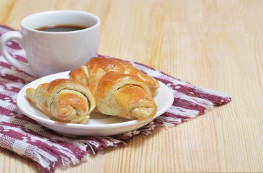 Ay çöreği bir tabak, peçete ile ışık ahşap bir masa üzerinde beyaz bir fincan kahve