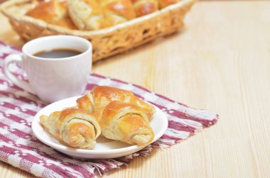 Ay çöreği, kruvasan sepeti, peçete ile ışık ahşap bir masa üzerinde beyaz bir fincan kahve ile beyaz plaka