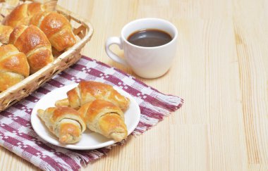 Ay çöreği bir plaka üzerinde ve bir sepet, peçete ile ışık ahşap bir masa üzerinde bir fincan kahve