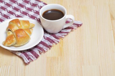 Bir fincan kahve bir peçeteye ahşap masa lambası üzerinde beyaz bir tabakta kruvasan