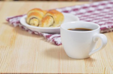 Bir fincan kahve bir peçete ahşap bir masaya yanında beyaz bir daire üzerinde iki ay çöreği