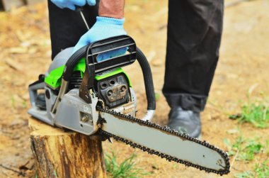 Mavi çalışma eldiven bir erkekte bir günlük, bir yakın çekim fotoğraf sprey bir chainsaw başlattı