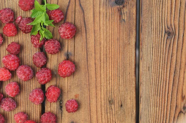 A chalk of mint lies among the raspberry berries on a wooden background