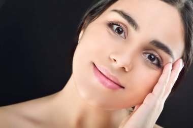 Güzel genç kız elini nazikçe yanağının yakınında tutuyor. Siyah arkaplanda stüdyo çekimi