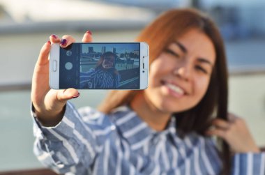 Sokakta uzanan eliyle selfie çeken güzel esmer bir kızın portresi.
