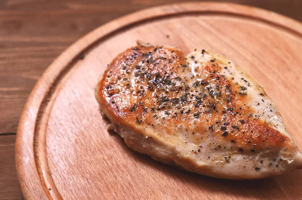 Fried chicken fillet on a board sprinkled with spices: salt and pepper, side view