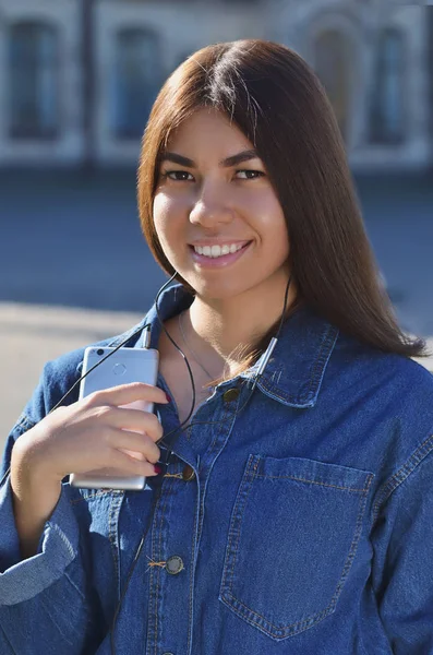 Retrato de uma jovem, aparência asiática vestida com uma jaqueta de ganga com um telefone em suas mãos — Fotografia de Stock