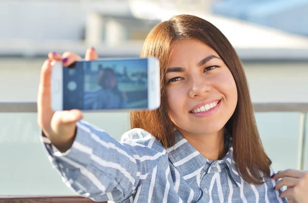 Joven hermosa chica hace selfie y ella está sentado en un banco en la ciudad —  Fotos de Stock